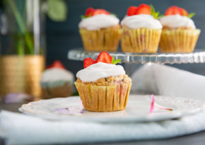 Strawberries and Cream Cupcakes on a glass pedestal with a cupcake on a plate in front