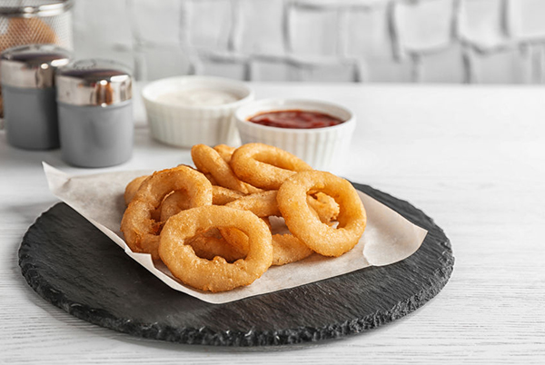 Slate plate with tasty onion rings on table