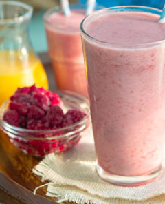 Pink colored detox smoothie on a wooden tray with smoothies in the background