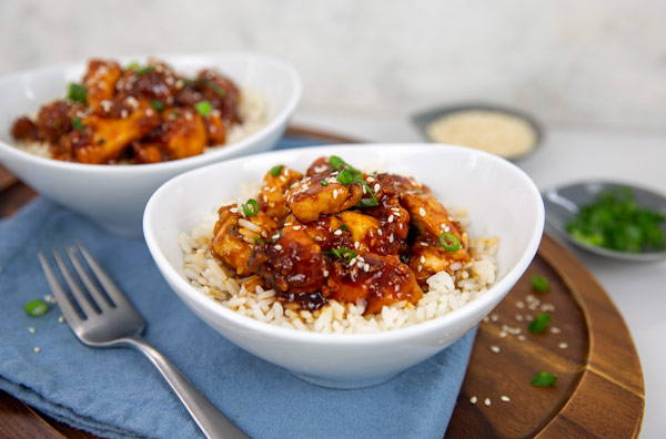 No-Fry Honey Sesame Chicken over rice in a white serving bowl