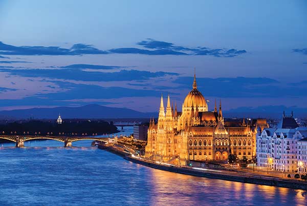 Budapest from the Danube River at sundown with the city lit up and the sky and water vibrant blue