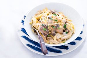 Chicken Tetrazzini in a white bowl on top of a white plate with dark blue streaks on it