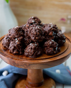 Chocolate Sunbutter Cookie Clusters on a wooden pedestal with a blue cloth napkin at the bottom and marshmallows in the background