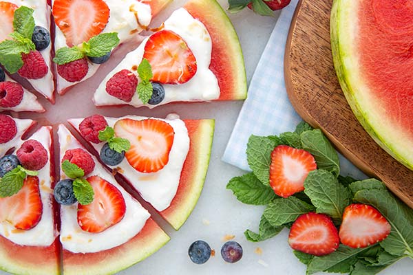 Round slice of watermelon cut into triangles to form a pizza, topped with yogurt and berries