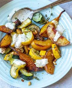 Roasted Summer Squash with Peaches and Pine Nuts on a white plate drizzled with a cream sauce