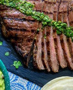 Carne Asada sliced into strips with chimichurri on top on a slate serving tray