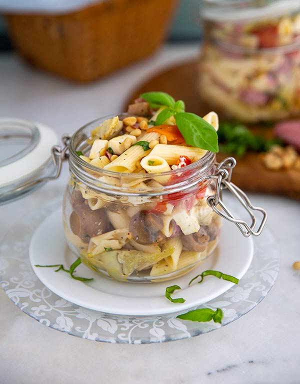 Summer Antipasto Pasta Salad in a glass jar set on top of a white plate