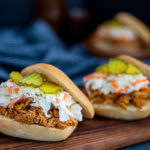 Closeup of Quick BBQ Chicken Sliders topped with slaw and pickles on a wooden serving board