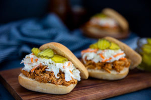 Closeup of Quick BBQ Chicken Sliders topped with slaw and pickles on a wooden serving board