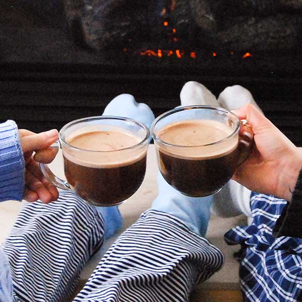 Couple holding mugs of BareLife Hot Cocoa in their pajamas in front of a fireplace