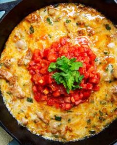 Overhead view of Queso Fundido topped with chopped tomatoes and cilantro in a black cast iron skillet