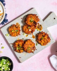Overhead view of Asian-Inspired Latkes on a wooden board with Asian dipping sauce in a decorative bowl on the side