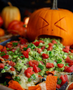 Carved pumpkin face with guacamole coming out of its mouth onto Halloween Nachos