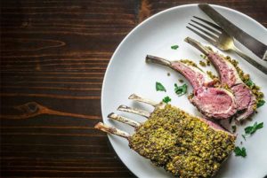 Overhead view of Pistachio Crusted Rack of Lamb on a white plate on a brown wooden background