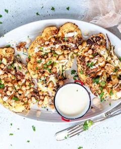Spiced Cauliflower Steaks on a white plate sprinkled with fresh herbs