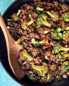 Overhead view of ground bison and broccoli skillet dinner in a black skillet with wooden spoon on a sky blue background