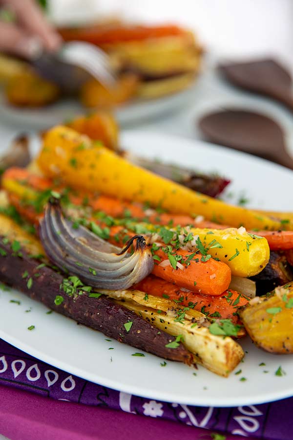 Roasted Root Vegetables with fresh herbs on top on a white platter with purple napkins underneath