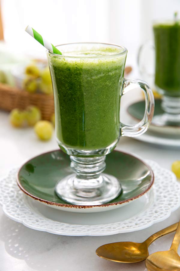 Mango Ginger Kale Smoothie with a green and white straw and green grapes in the background