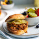 Sloppy Joes on a white plate with fresh sliced fruit in the background